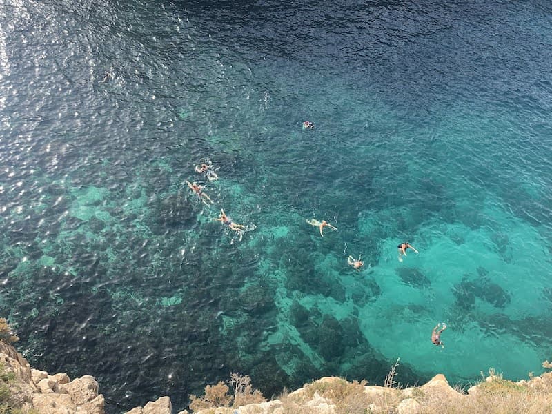 I Drove All Over Puglia, Italy — Here Are 6 Road Trip Itineraries That Actually Work High-angle view of people swimming and snorkeling in the turquoise waters of Lama Monachile Beach in Polignano a Mare, Puglia, Italy.