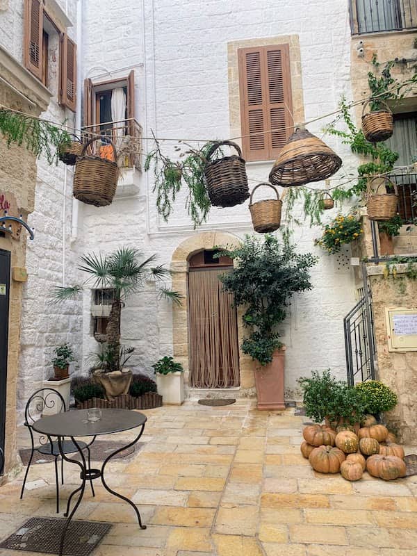 I Drove All Over Puglia, Italy — Here Are 6 Road Trip Itineraries That Actually Work Sunny courtyard in Polignano a Mare with wicker baskets, plants, and pumpkins
