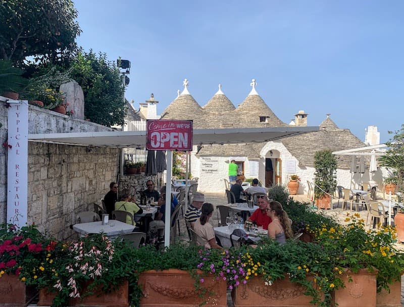 Outdoor dining area beside whitewashed trulli buildings in Alberobello, Italy