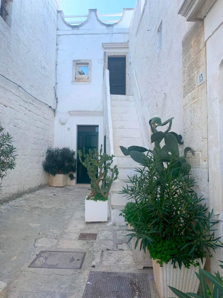 Sunlit whitewashed alley with traditional stone staircases in the historic center of Ostuni, Italy.