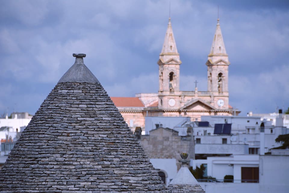 Trullo conical roof with Basilica of Saints Cosmas and Damian bell towers, Alberobello, Italy