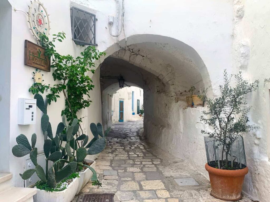 Whitewashed stone alleyway beneath a curved arch in Ostuni historic center, Puglia, Italy