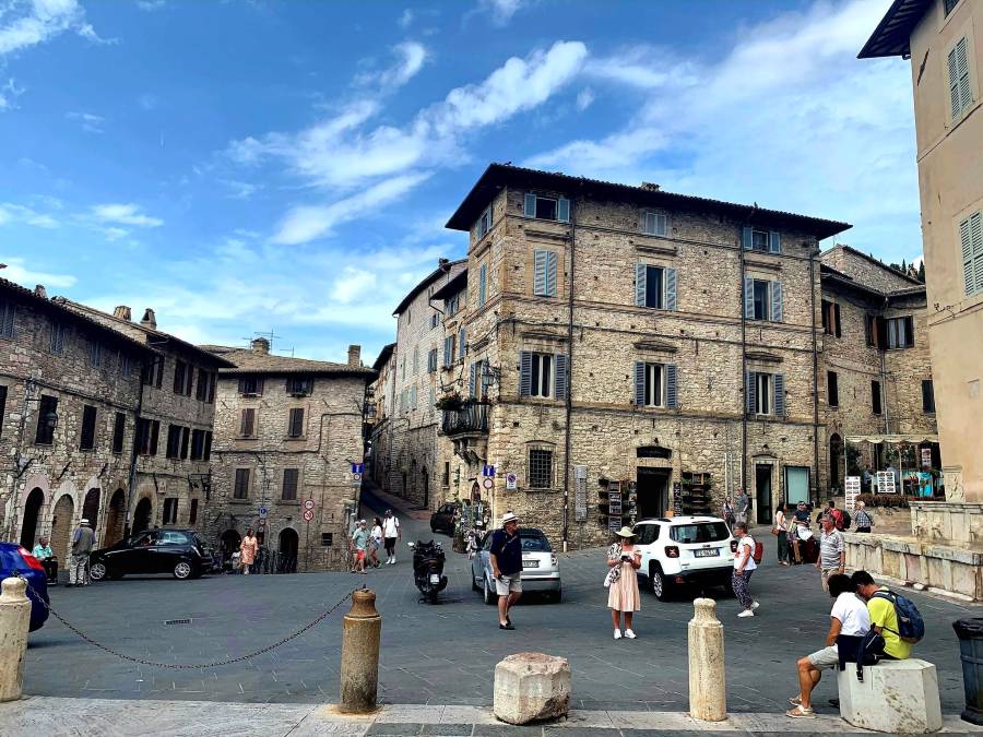 Sunny view of Piazza Inferiore di San Francesco with stone architecture near the lower entrance of the Basilica of St Francis in Assisi, Italy.