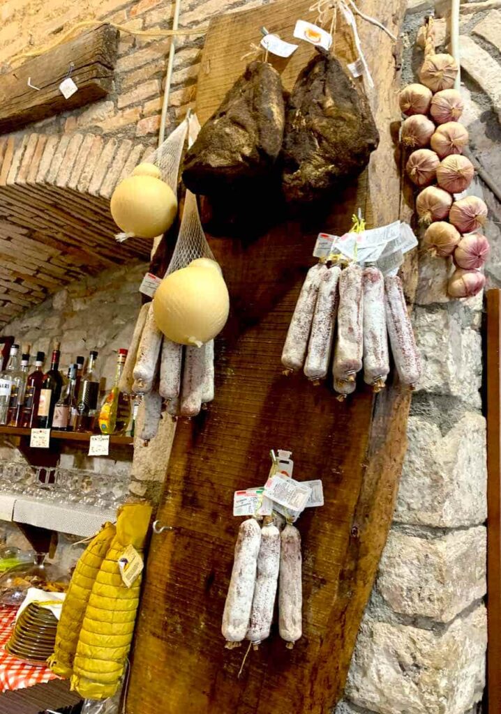 Traditional Umbrian food shop in Gubbio, Italy, with hanging cured meats, cheeses and a string of garlic